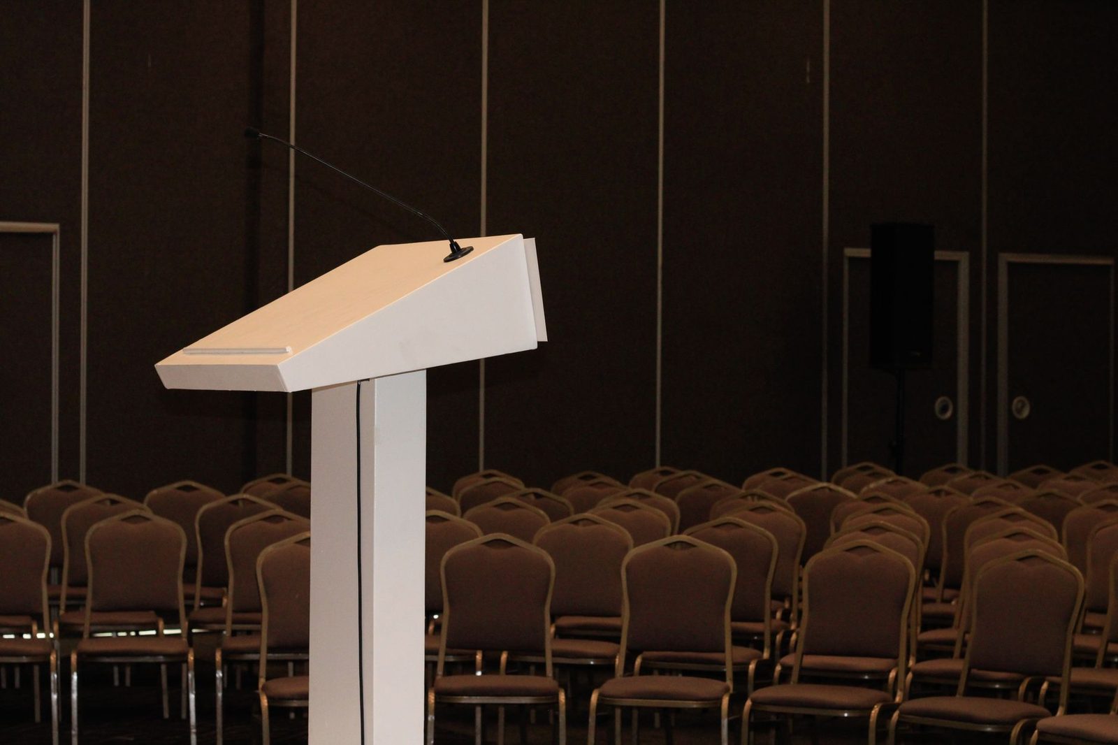 Empty conference podium with microphone facing rows of chairs — the platform of authority